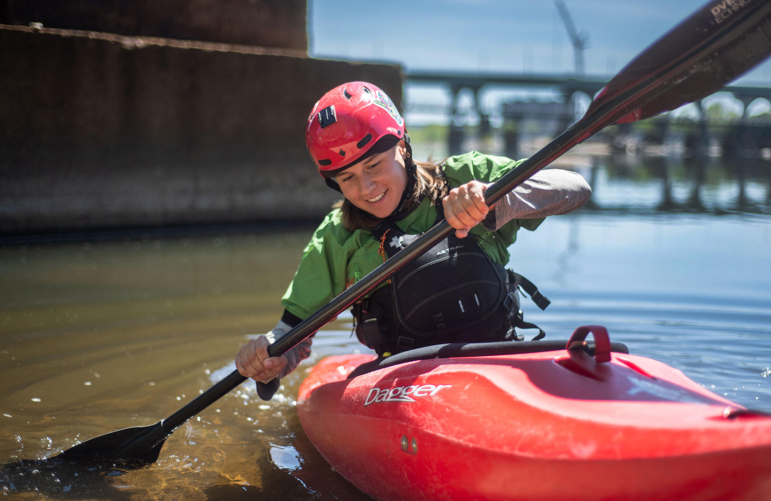 A photo of a woman paddling on a kyak in a river. 