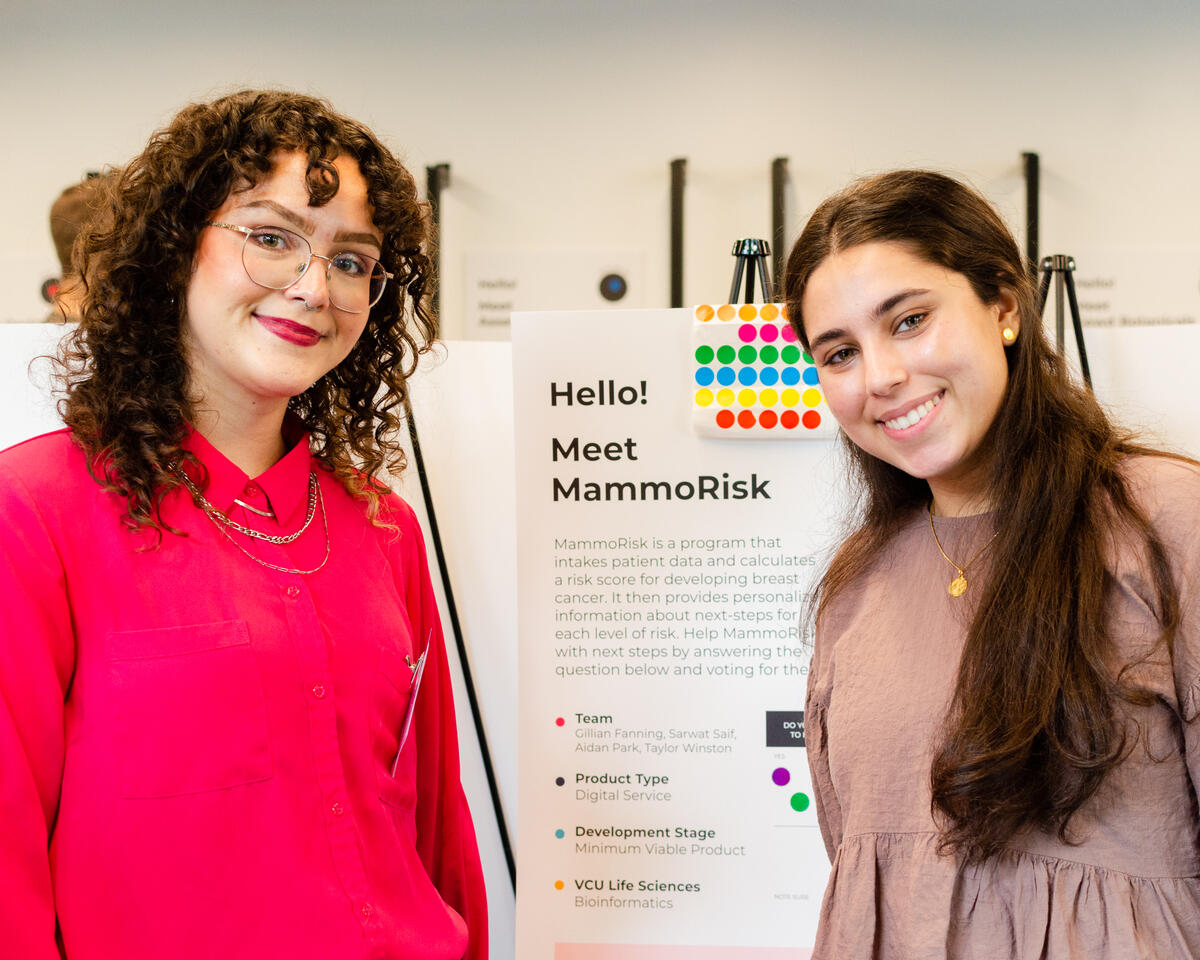 Two women smiling in front of a poster with details about a project called MammoRisk.