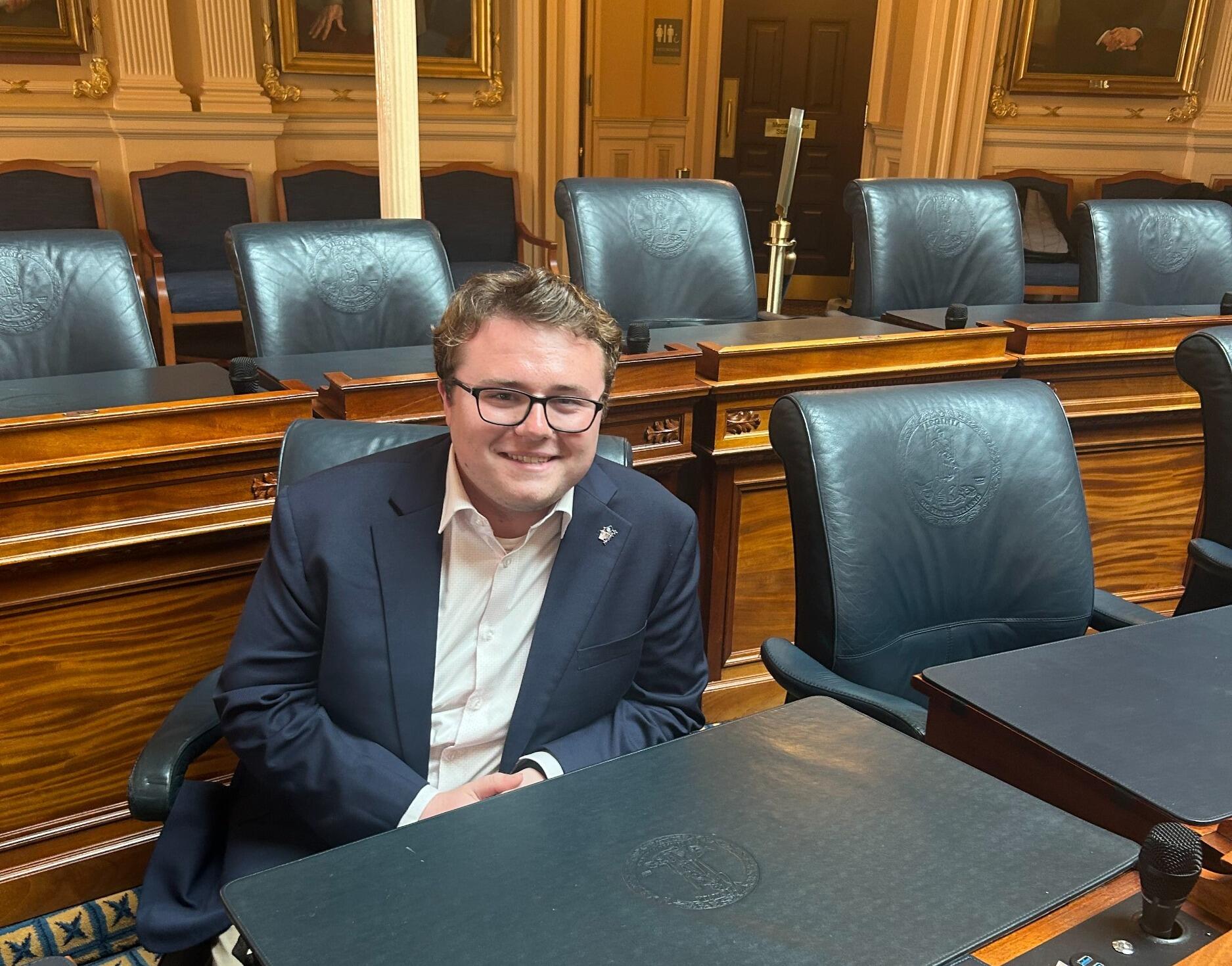 A photo of a man sitting behind a legislative desk. 