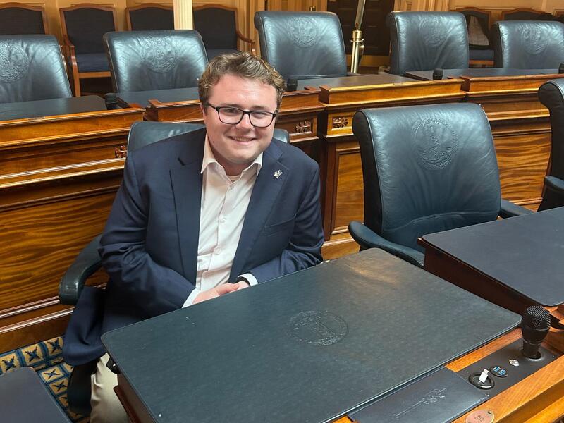A photo of a man sitting behind a legislative desk. 