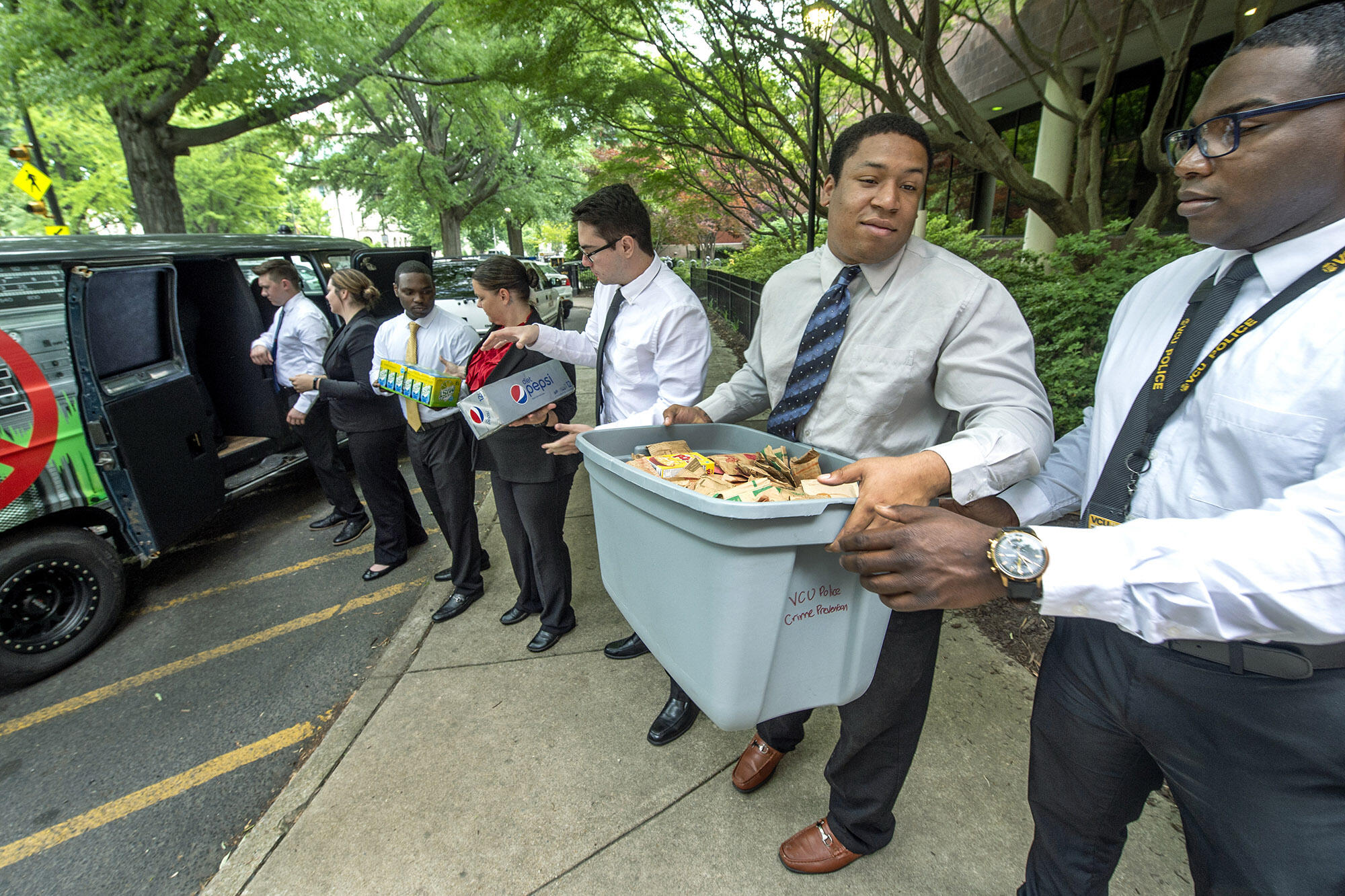 A line of people in business attire hand down packages and bins of food, starting at a van.