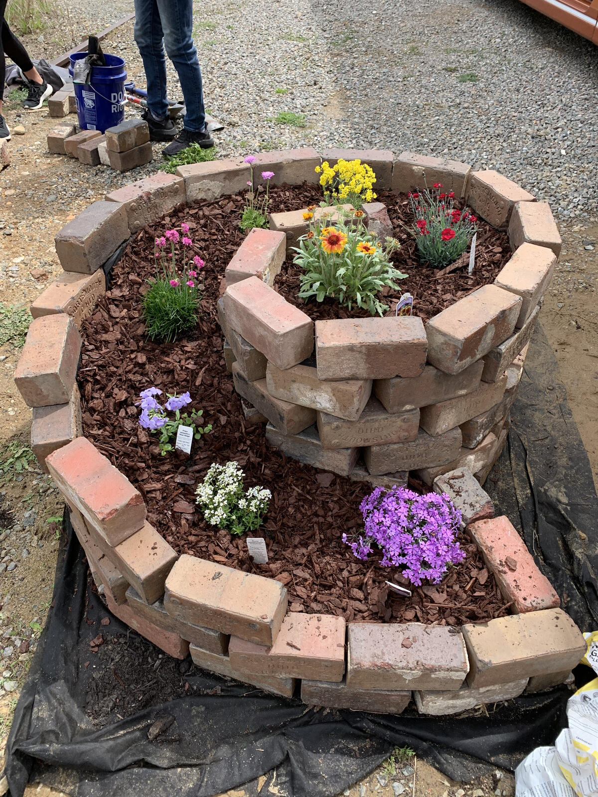 A spiral shaped planter made out of bricks with multicolored flowers going up along the spiral