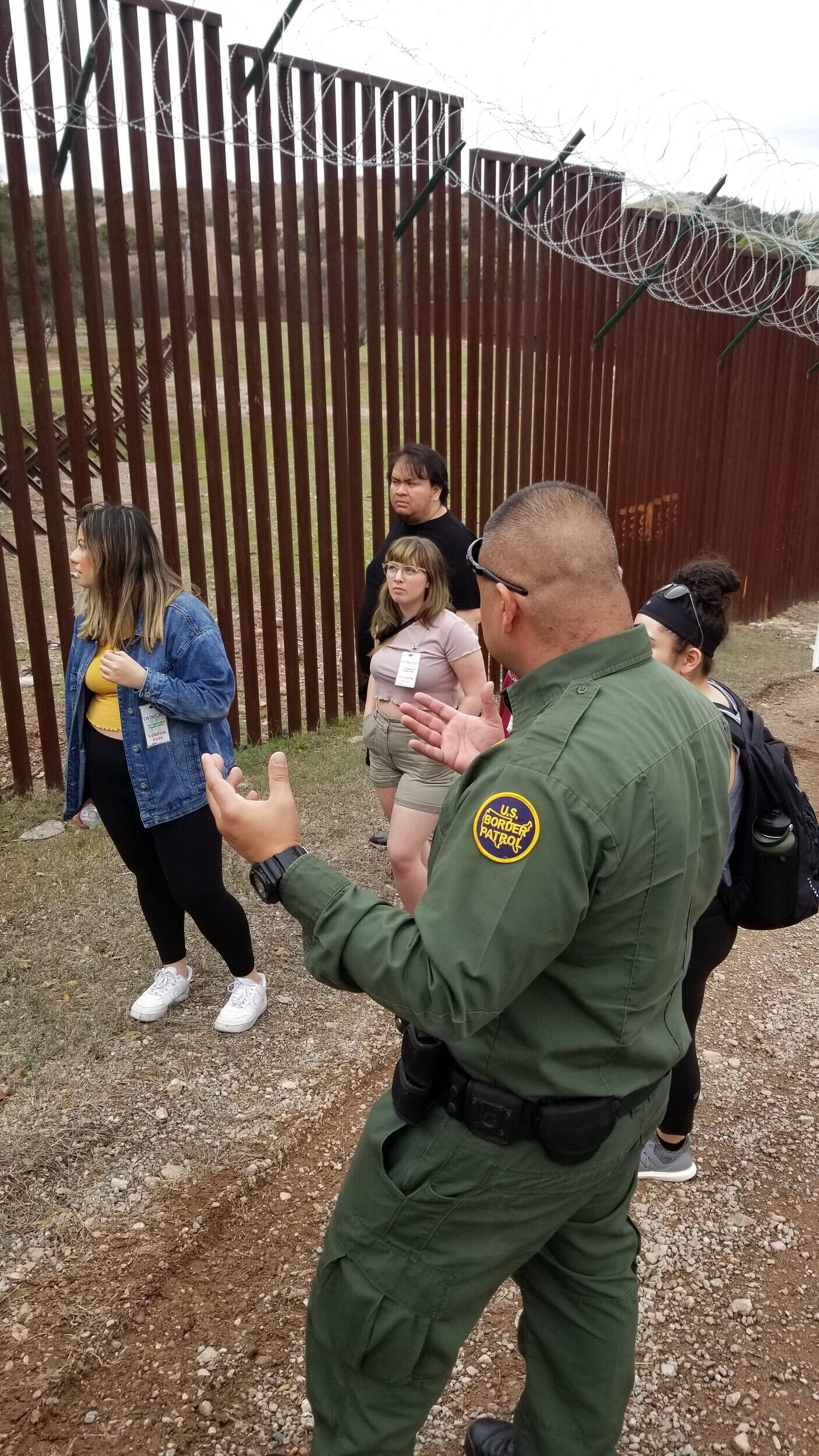 Students listen to a Border Patrol agent at the U S Mexico border wall.