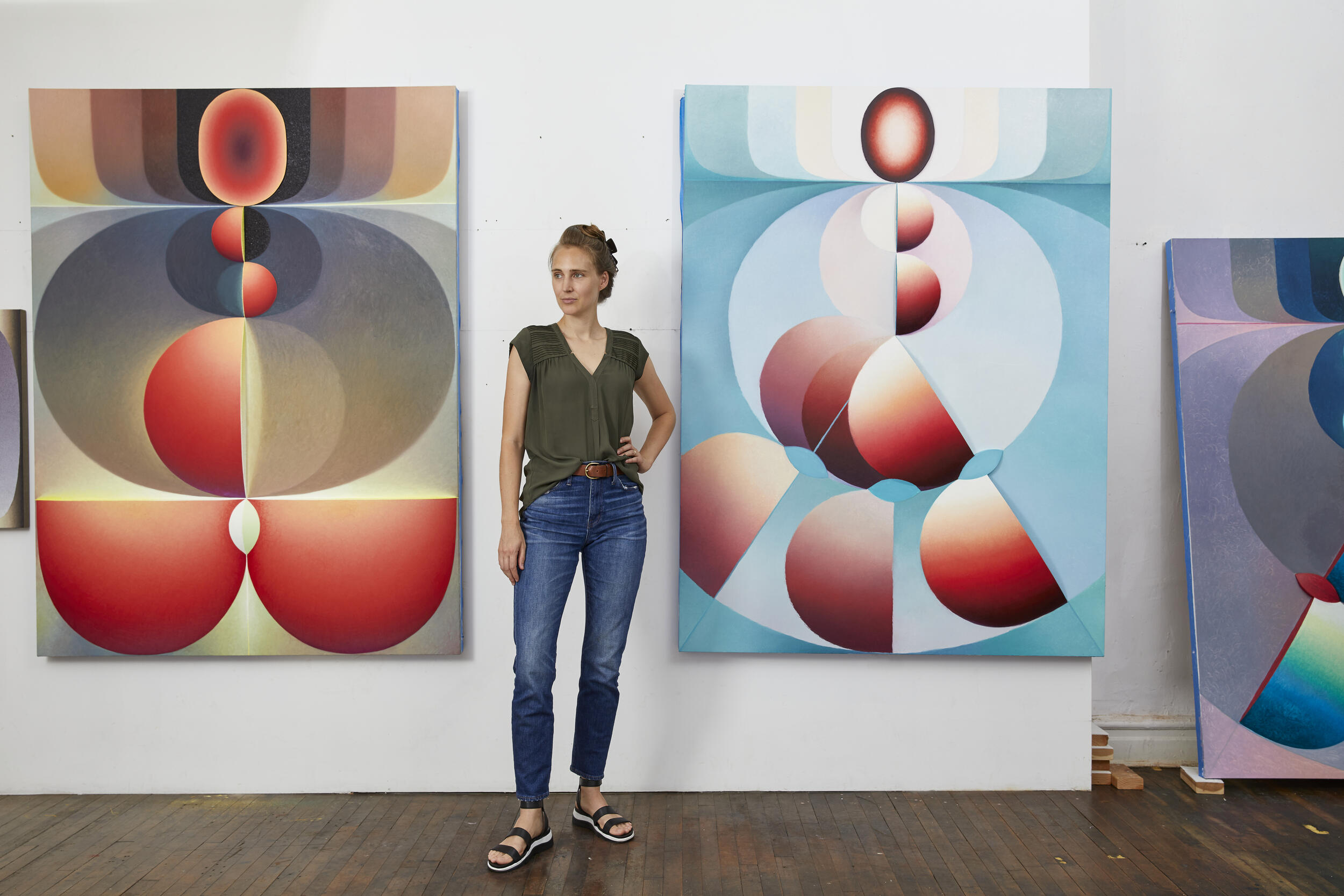A photo of a woman standing in between two geometric paintings. 