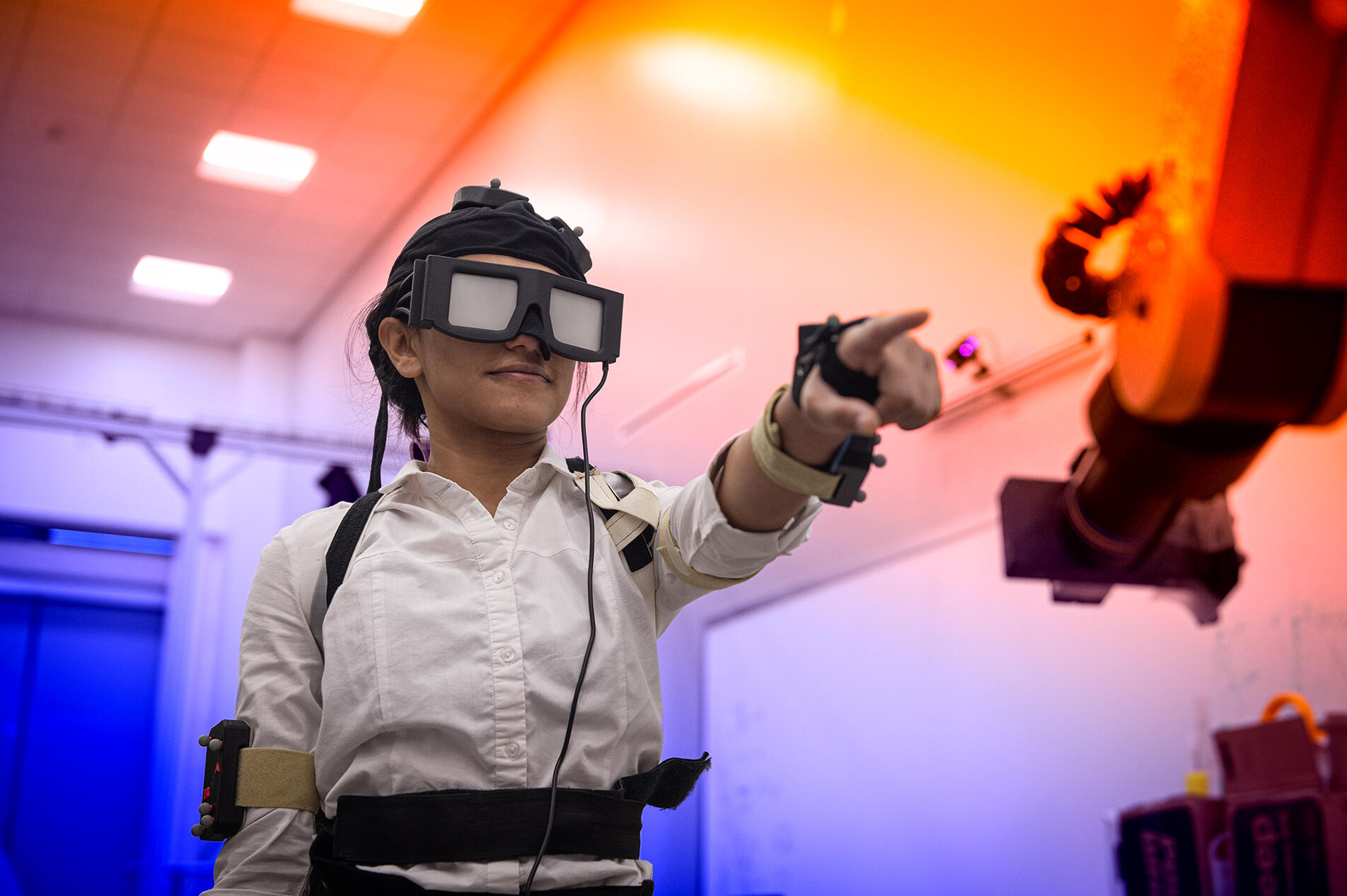 A photo of a person wearing gear to control a robotic arm with the arm in front of them. 
