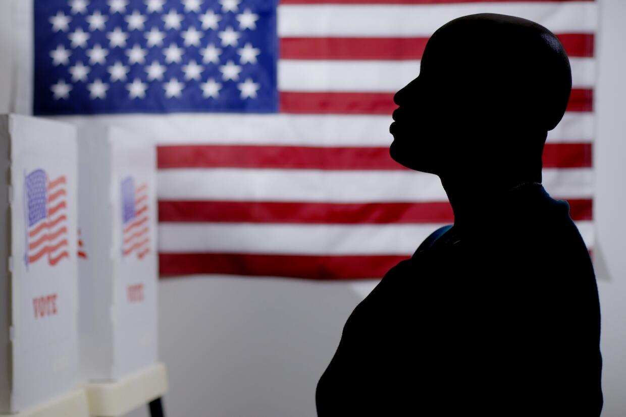 A silhouetted individual standing in front of voting booths.