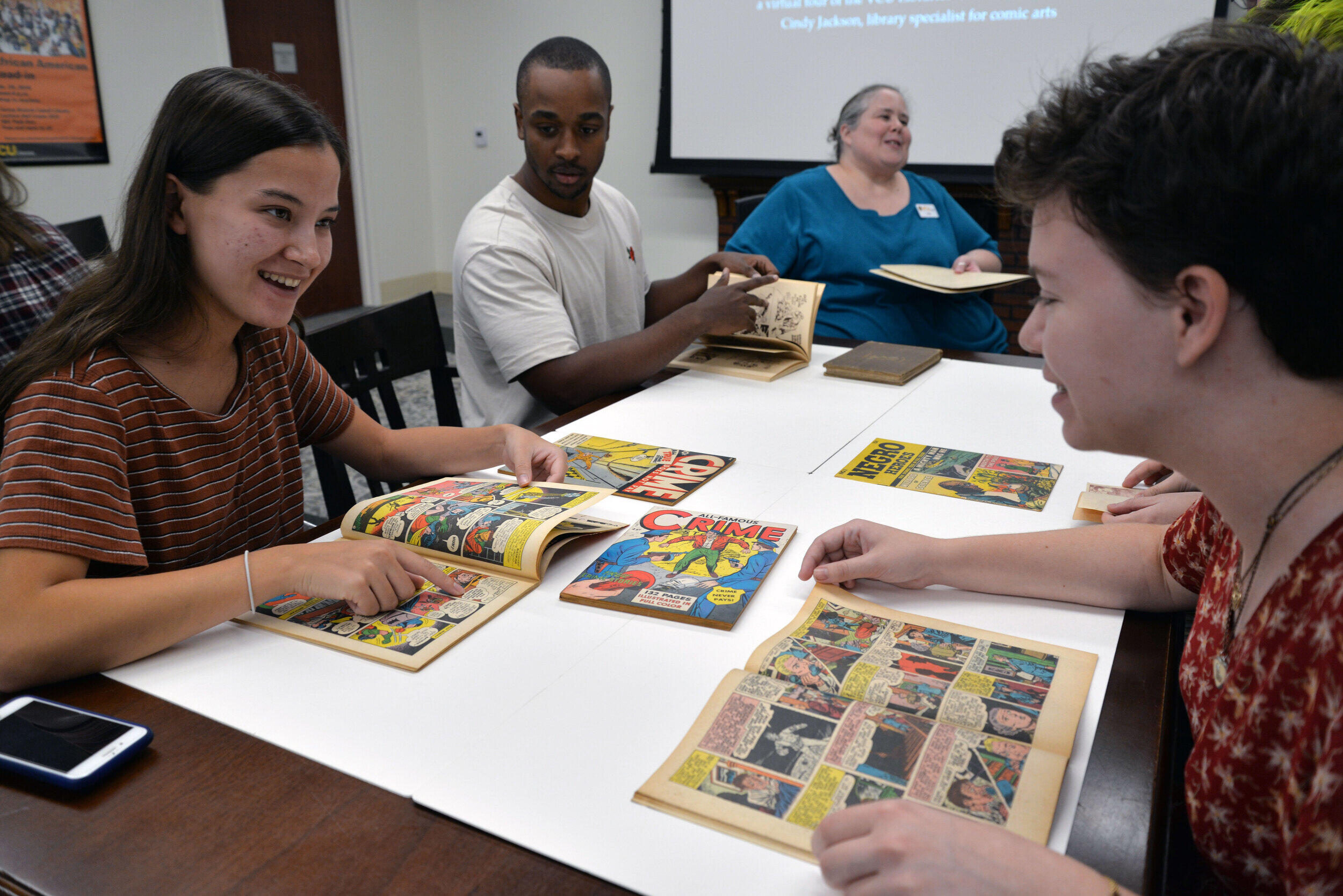 Three students seated at a table reading comic books.