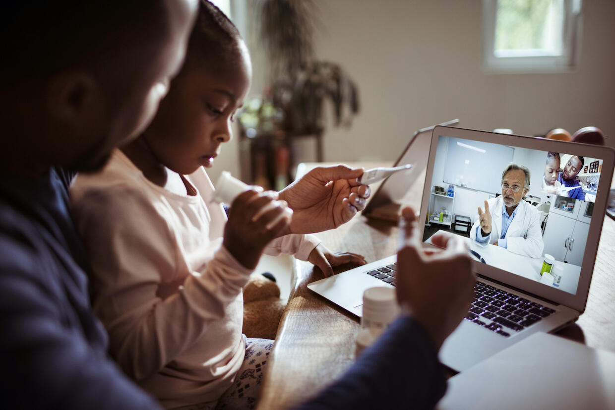 A parent and child participate in a teleconference session with a teacher.