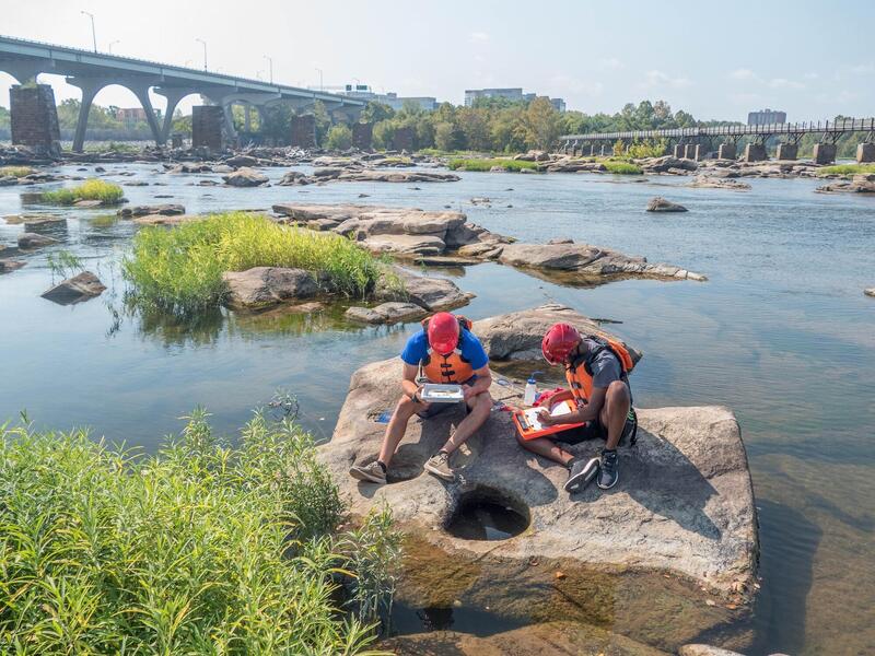 VCU students take samples from water pools collecting on rocks on the James River. (James Vonesh, for VCU News)