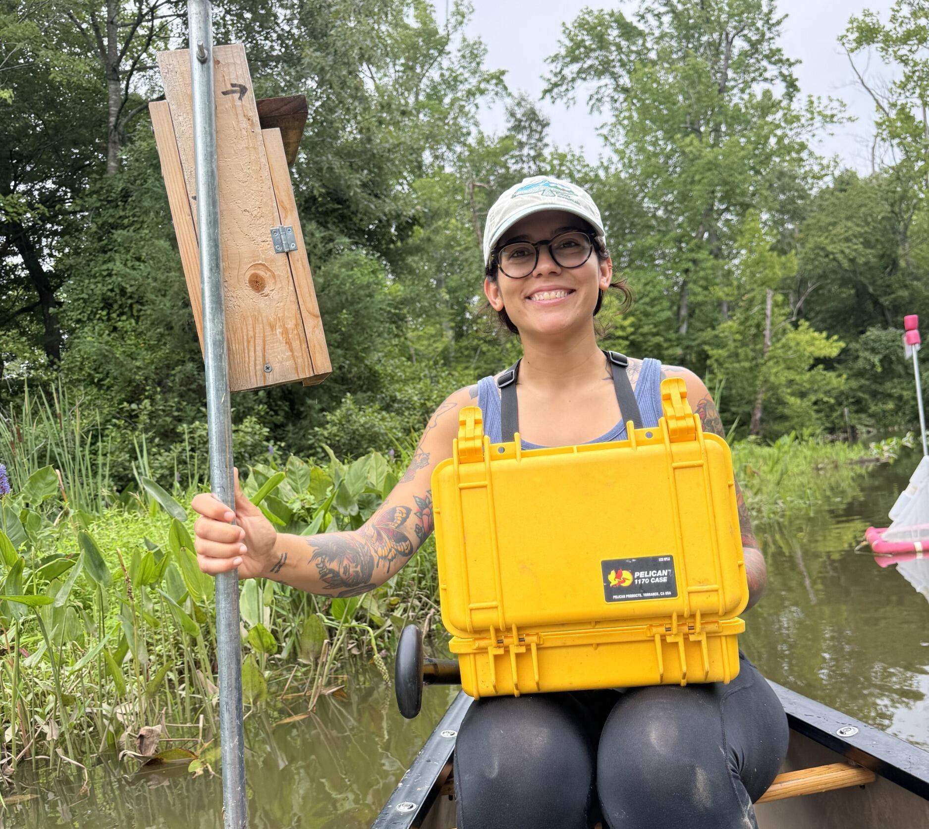 A photo of a woman sitting on a boat with a yellow box on her lap. 