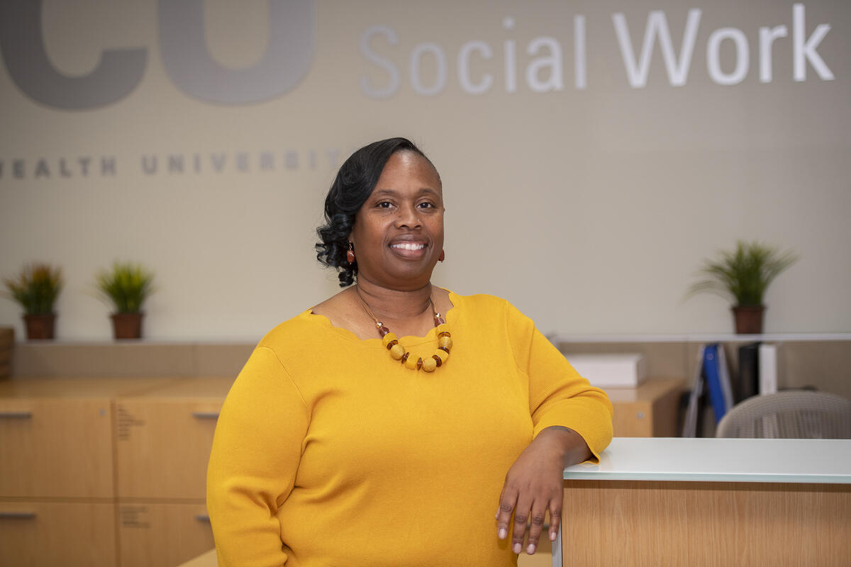 Shenita Williams leaning on a desk in front of a wall that says \"Social Work\" in silver letters. 