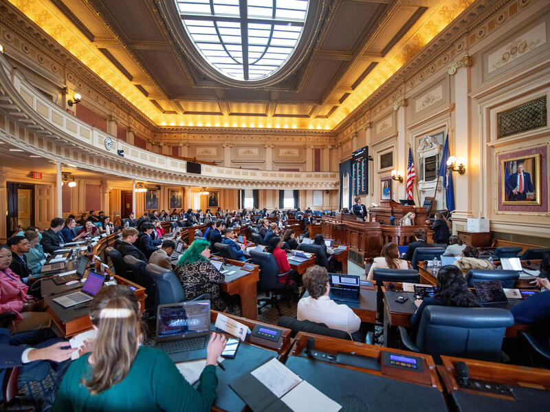 A photo of the floor of the Virginia House of Delegates Chamber filled with college students sitting at the desks. 