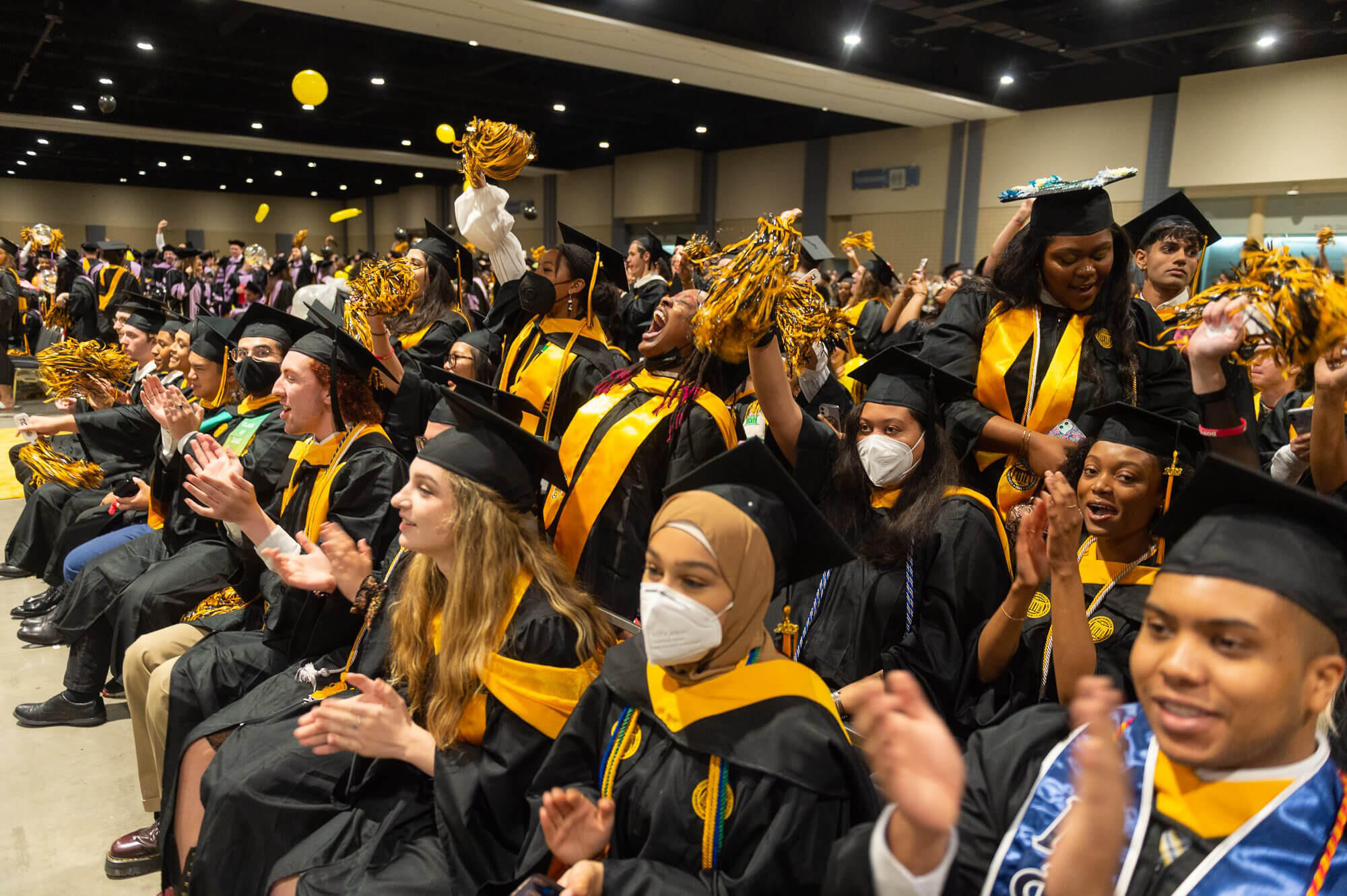 A group of students in graduation regalia sitting and clapping 