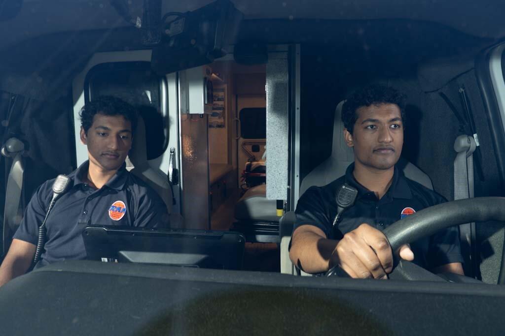 A photo of two men sitting in the front of an ambulance