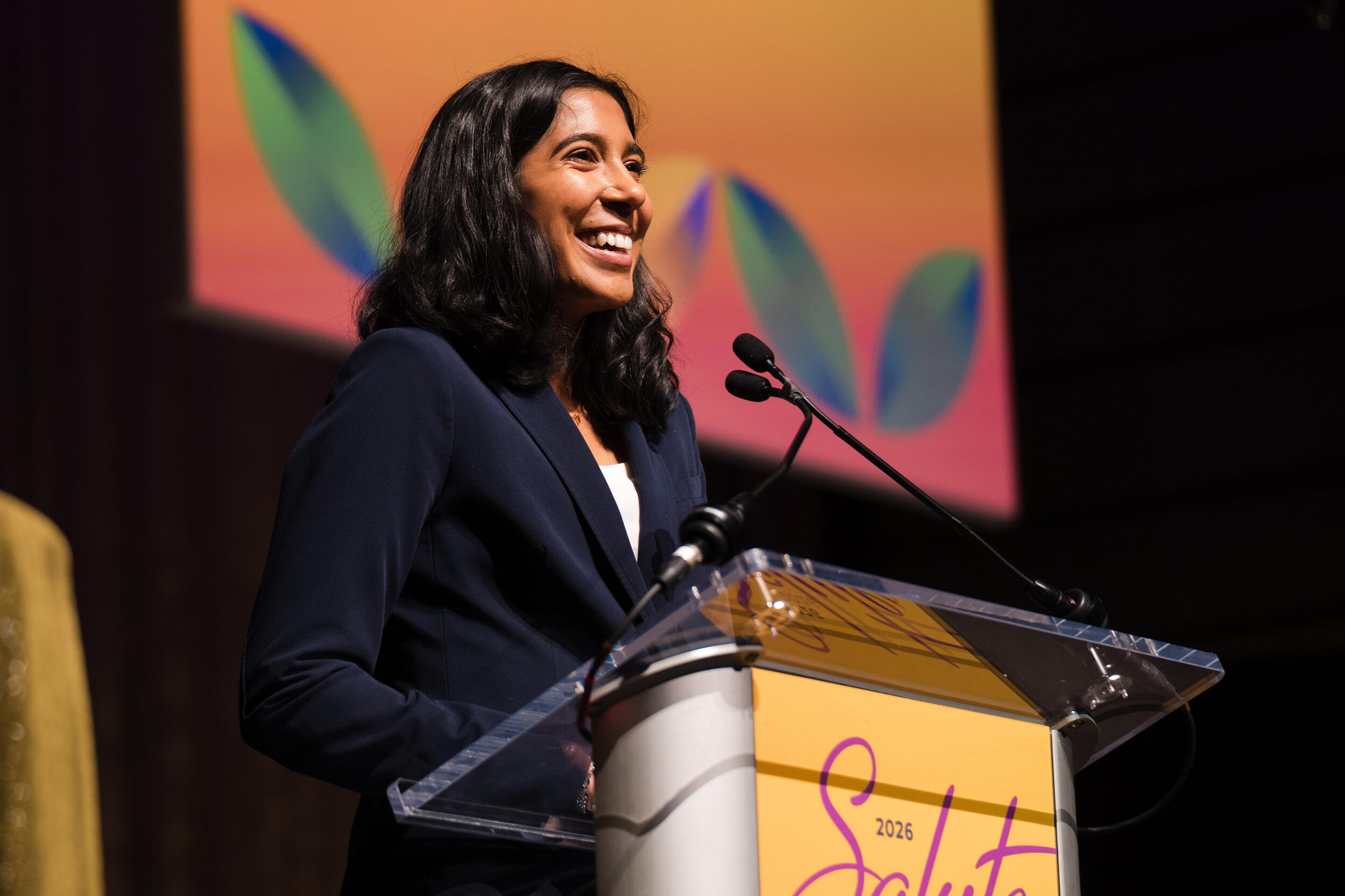 A photo of a woman standing behind a podium and smiling. 