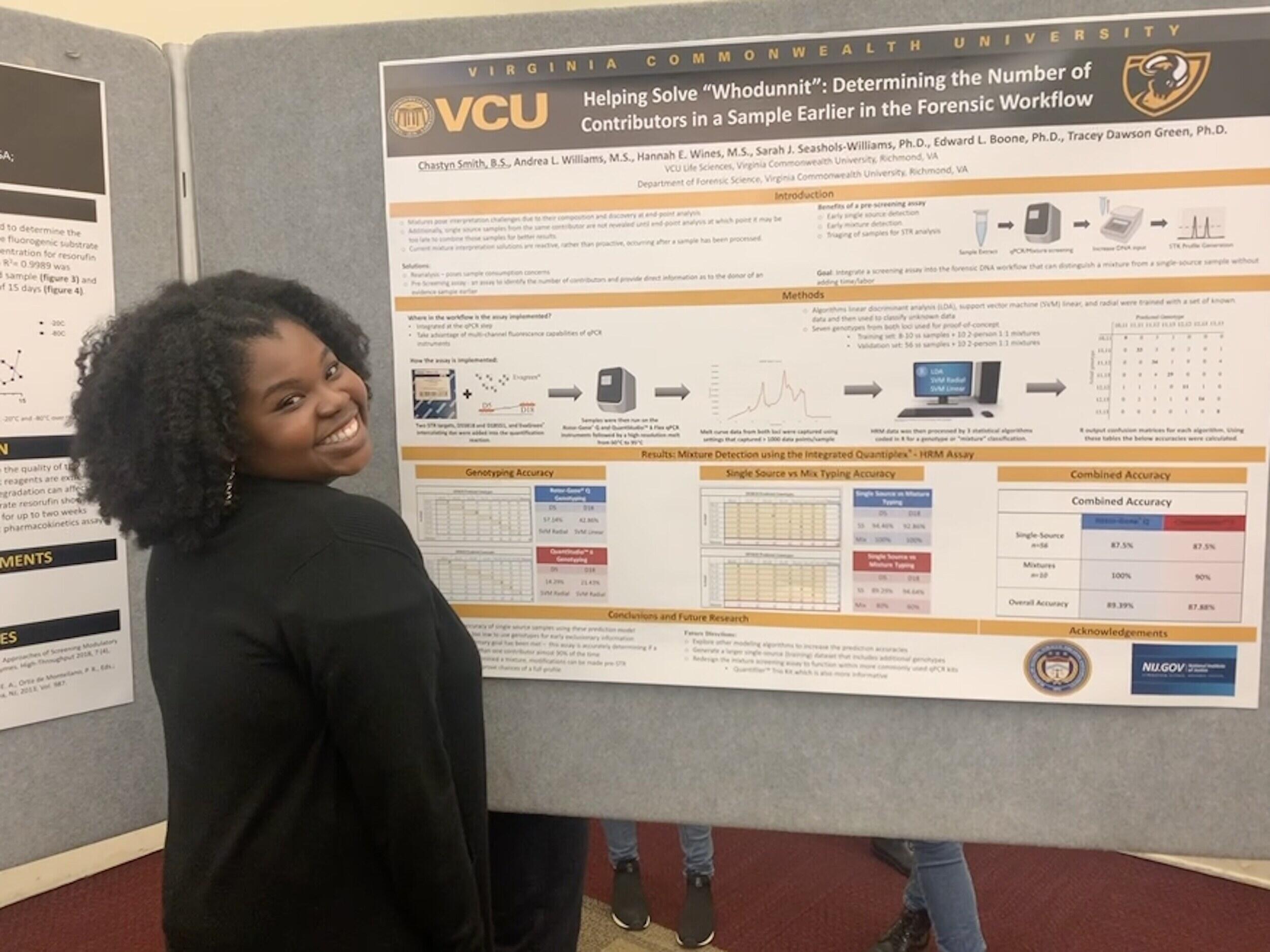 A woman smiling in front of a poster with research information on it 