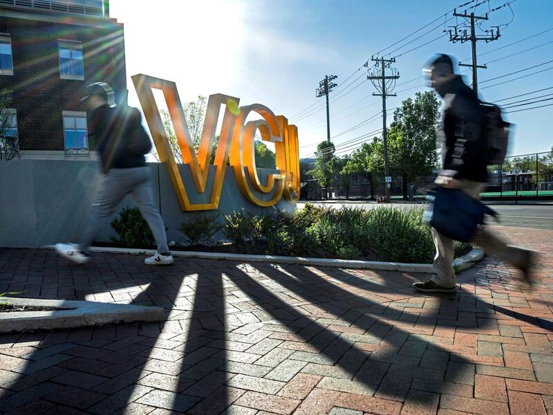 People walk outdoors past a large yellow VCU sign.