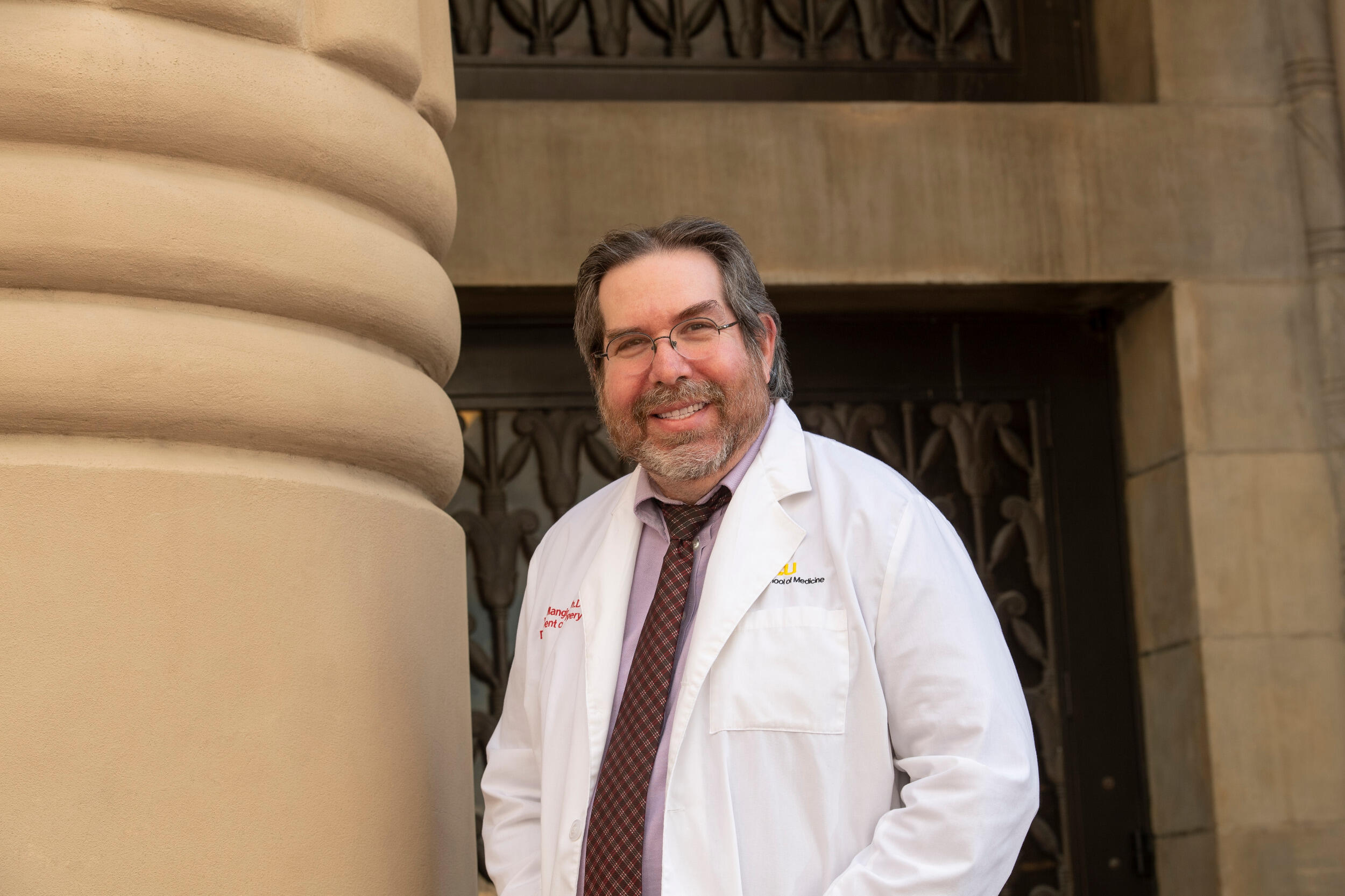 Image of Martin Mangino smiling in a lab coat and tie near a column.