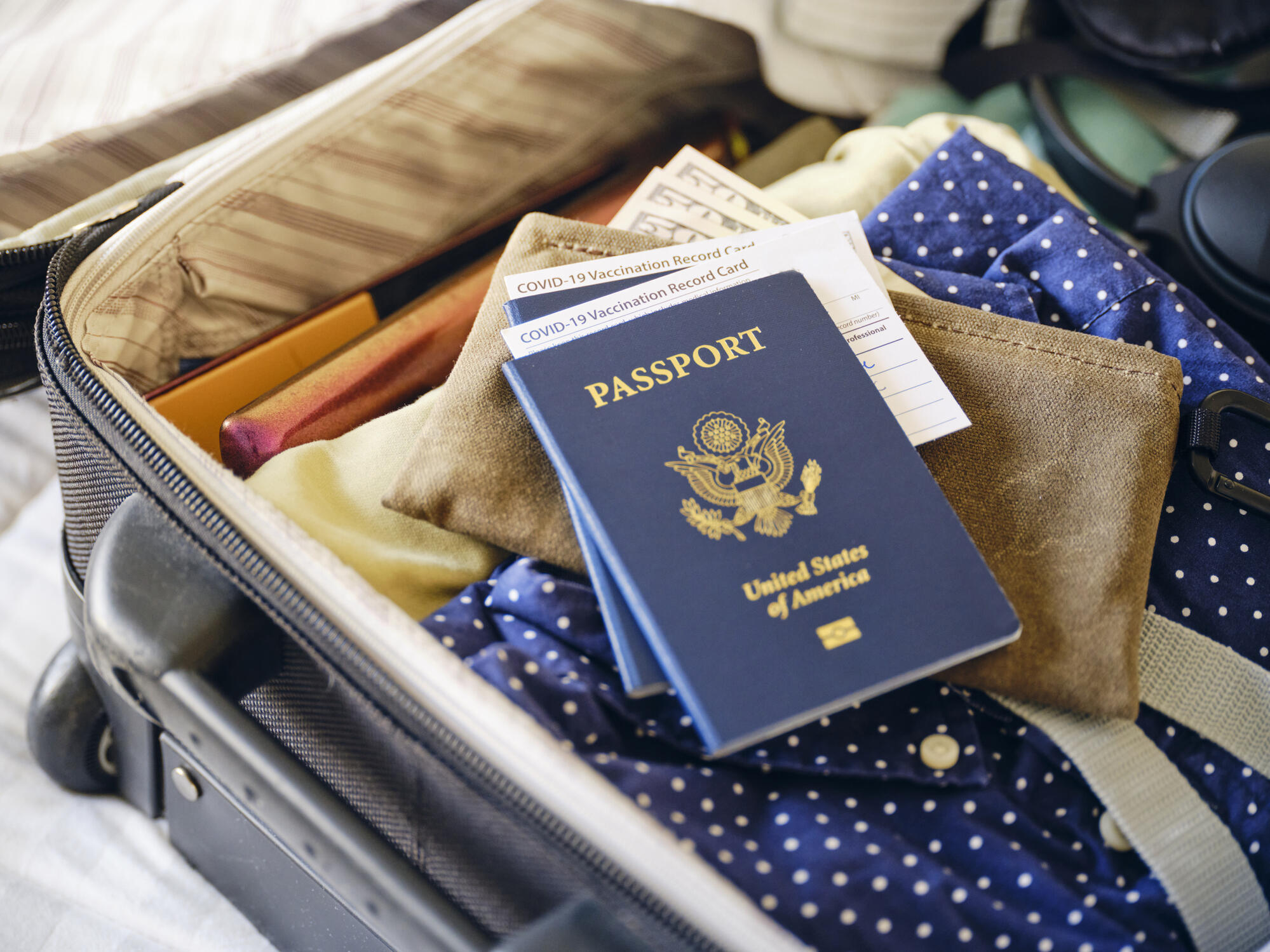 A passport sitting on top of an open suitcase filled with clothing. 