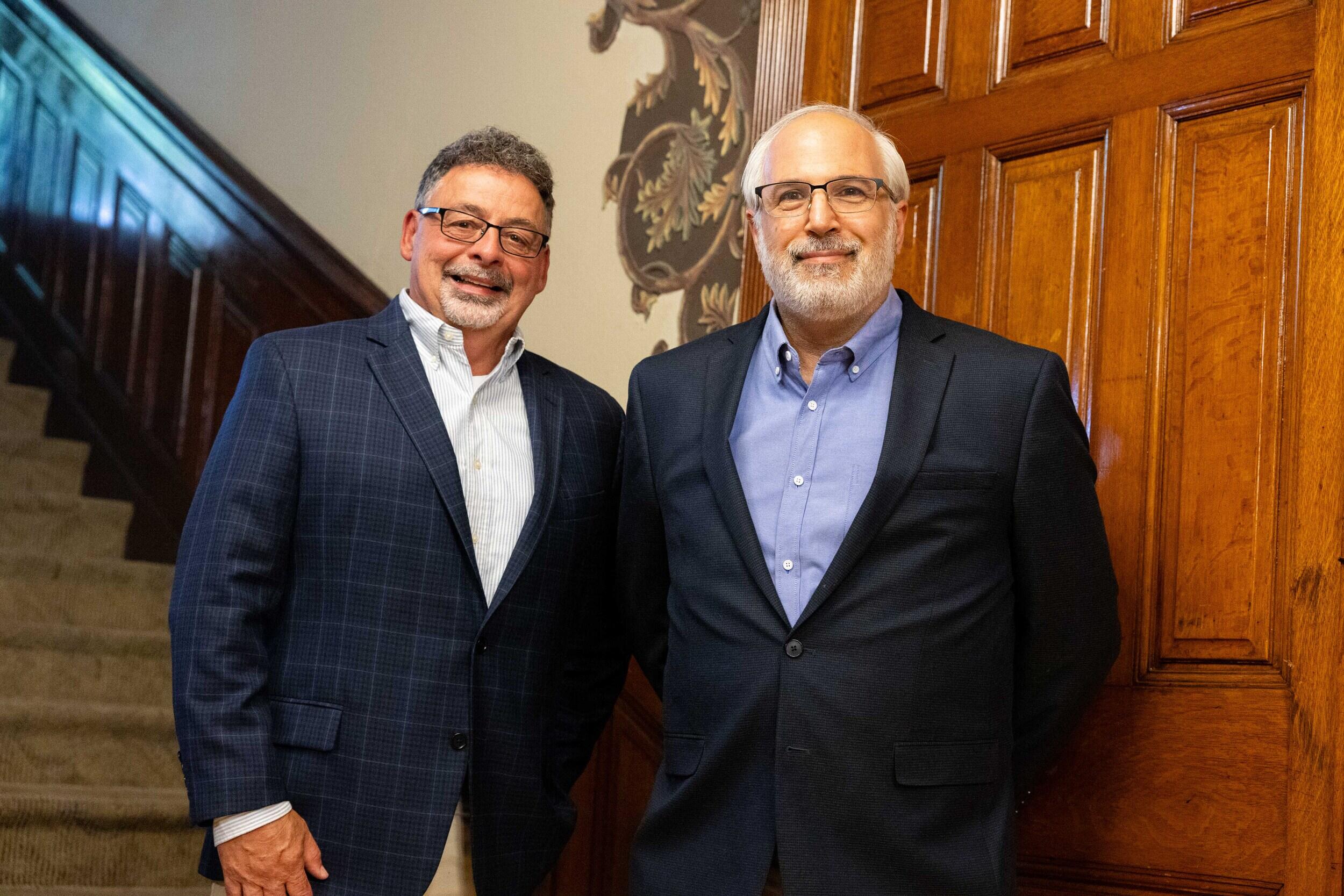 A photo of two men standing by a staircase. 