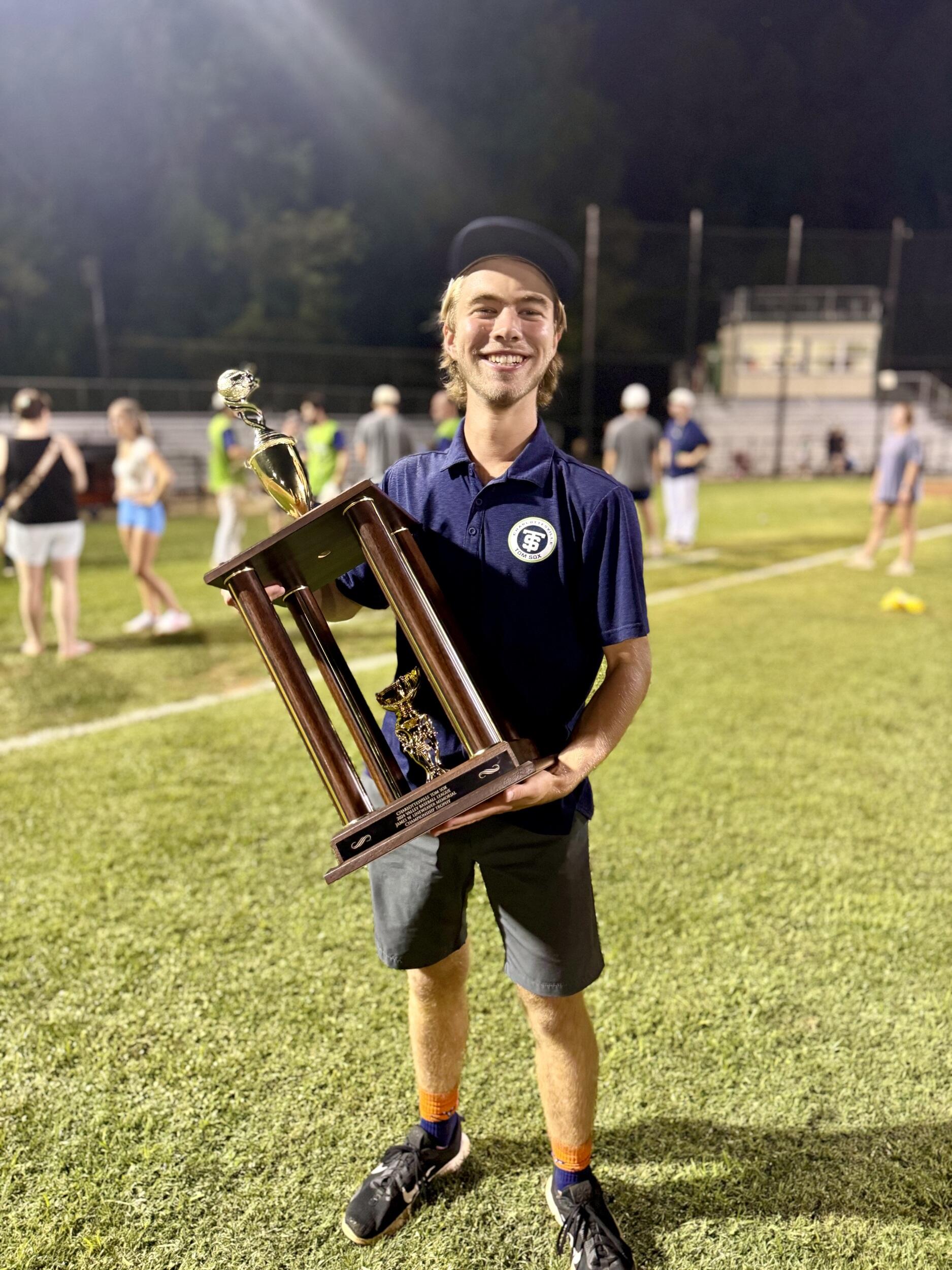 A photo of a man standing on a field holding a large trophy. 