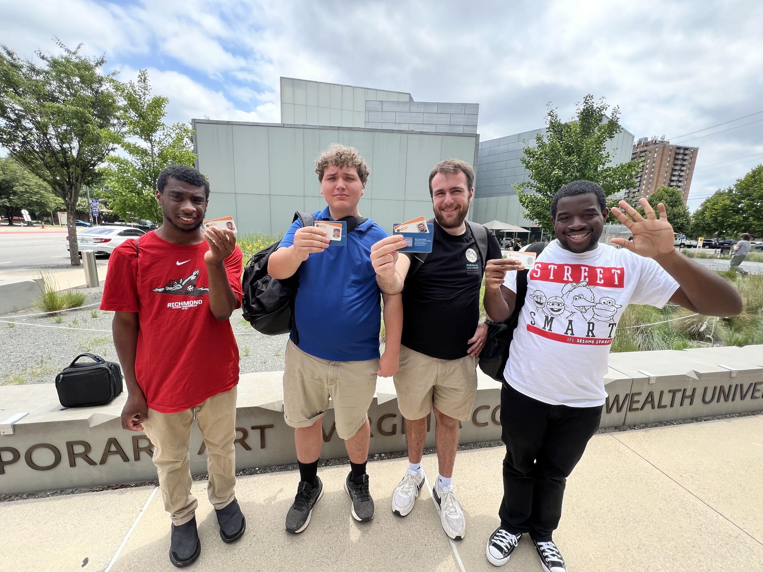 A photo of four men standing next to each other. They are all holding up a VCU ID card