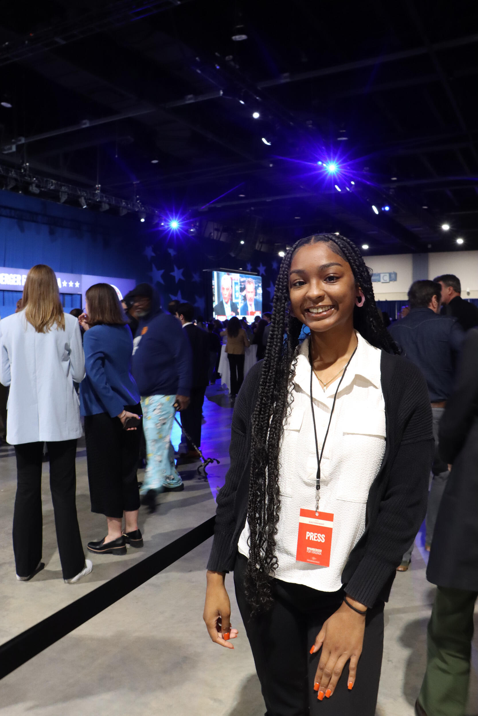 A photo of a woman from the knees up. Behind her is a crowd of people. 