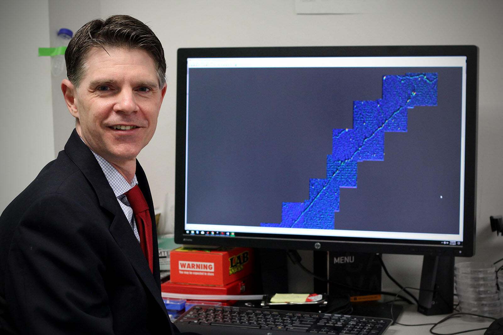 Man standing in front of large computer screen with a depiction of DNA strand displayed.