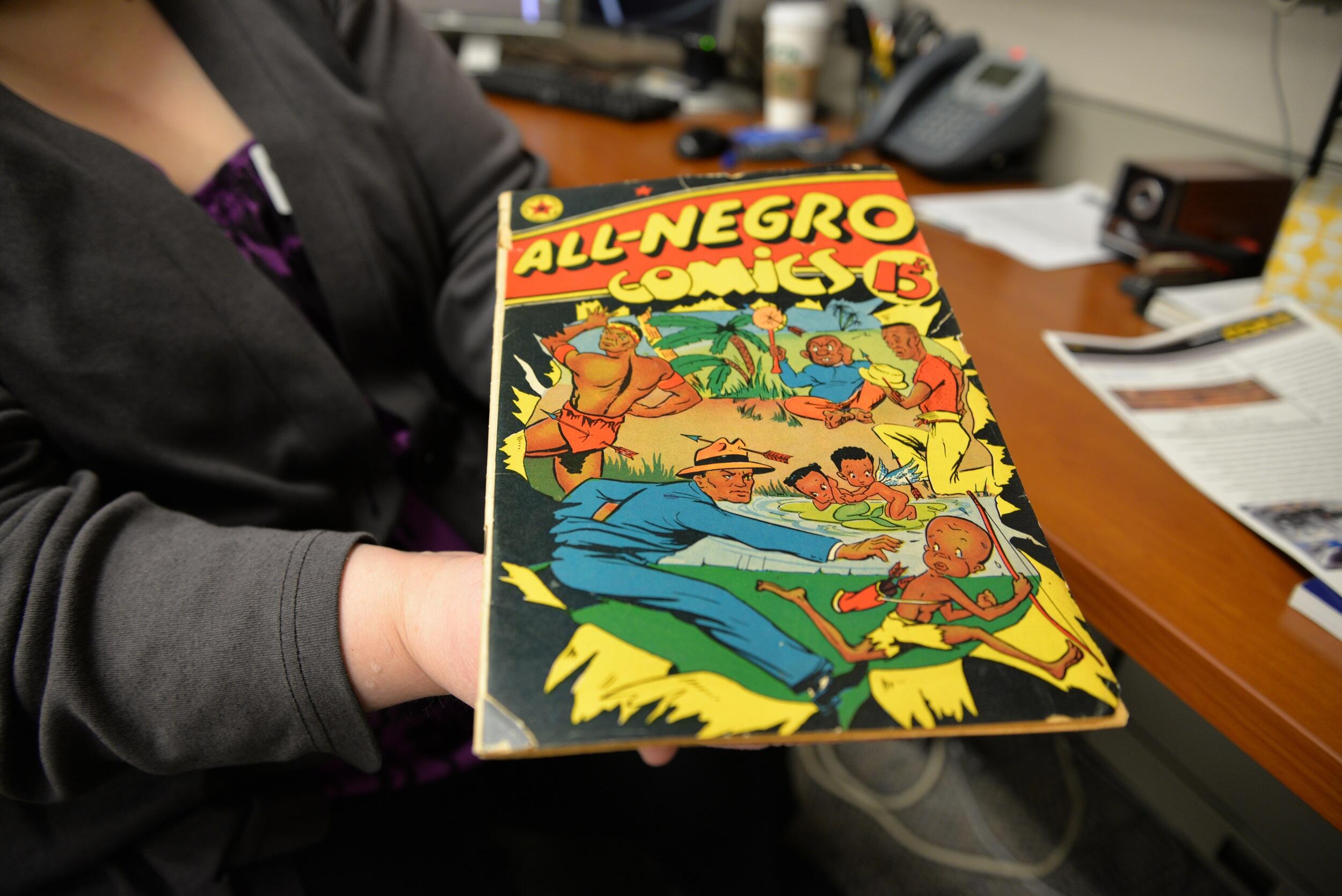 A photo ot a person holding out a comic book to show it. The cover says \"ALL-NEGRO cominics\" and has an image of a man chasing after a child.