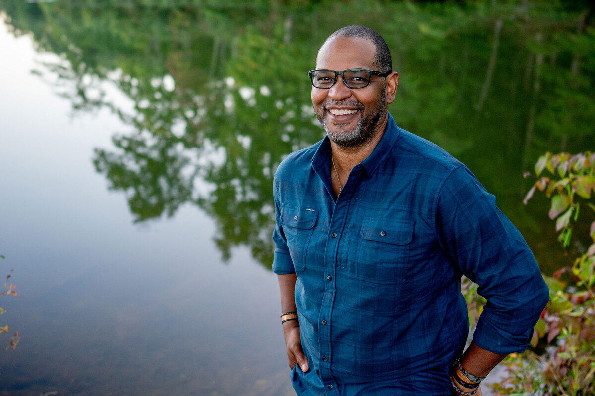 A photo of a man standing next to a lake while smiling. 