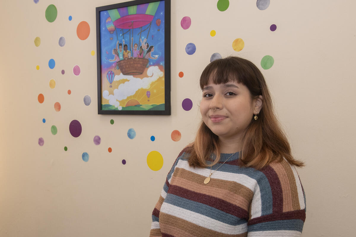 A woman standing in front of a wall with a picture hung up and colorful dots surrounding it. 
