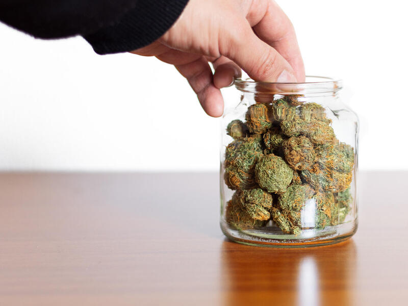 A photo of a hand reaching into a jar full of marijuana nuggets. 