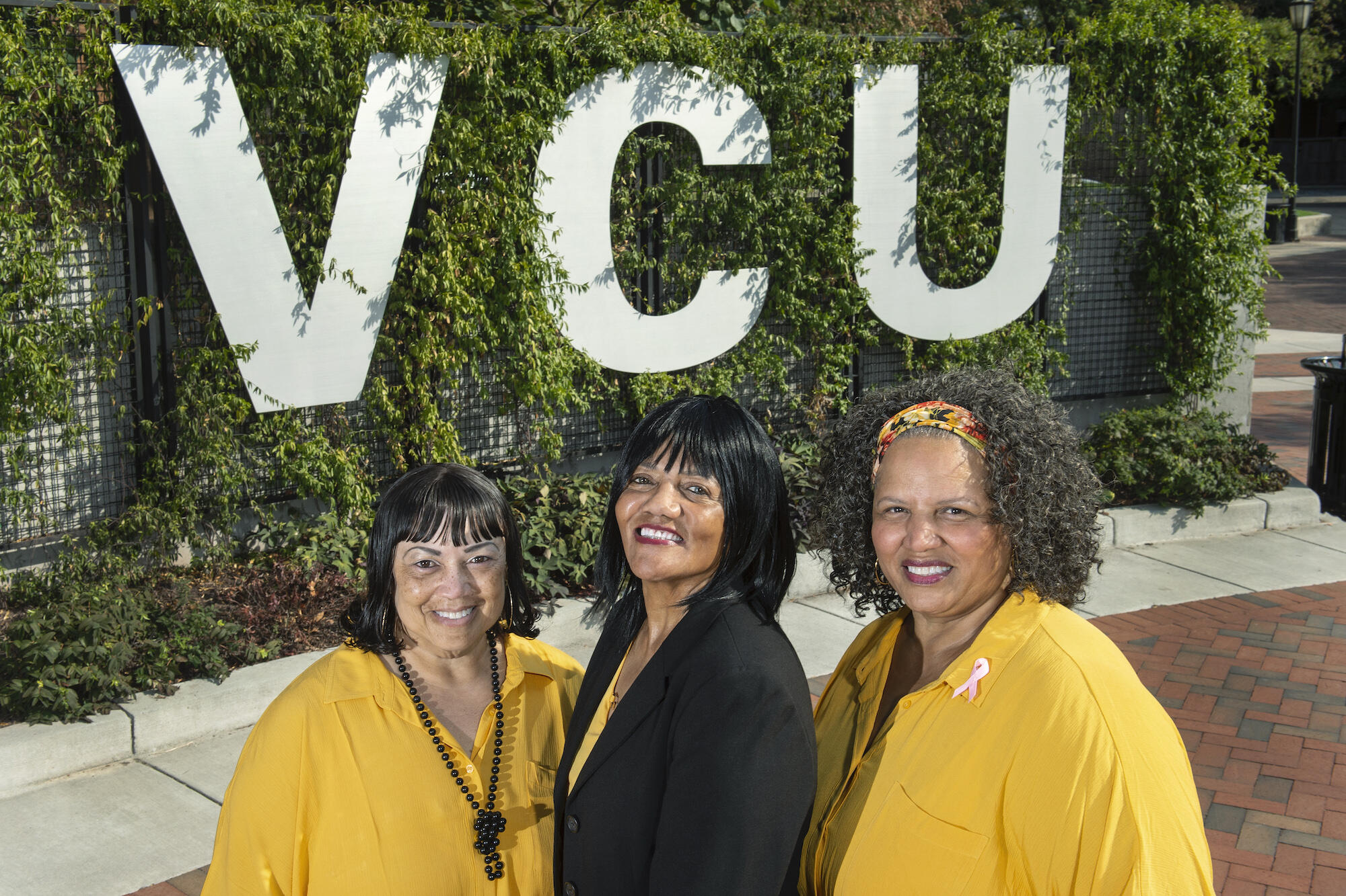 Three sisters stand in front of VCU signage. 