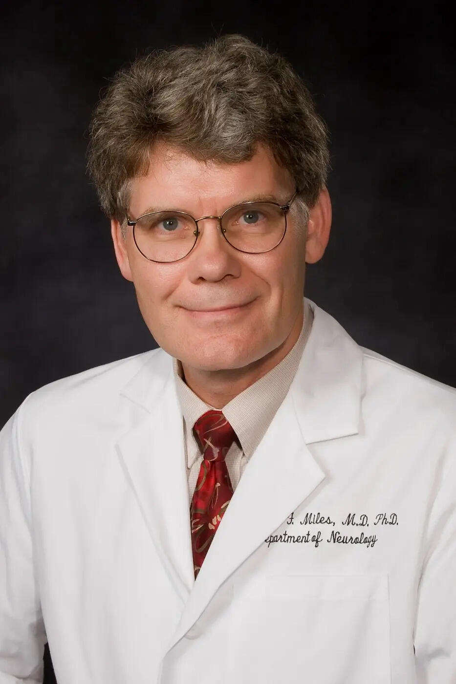 A portait of a man wearning glasses and a white lab coat. 