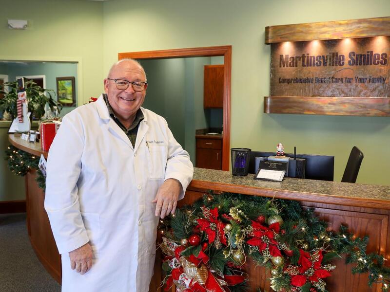 A photo of a man wearing a white medical coat standing next to a check in desk. 