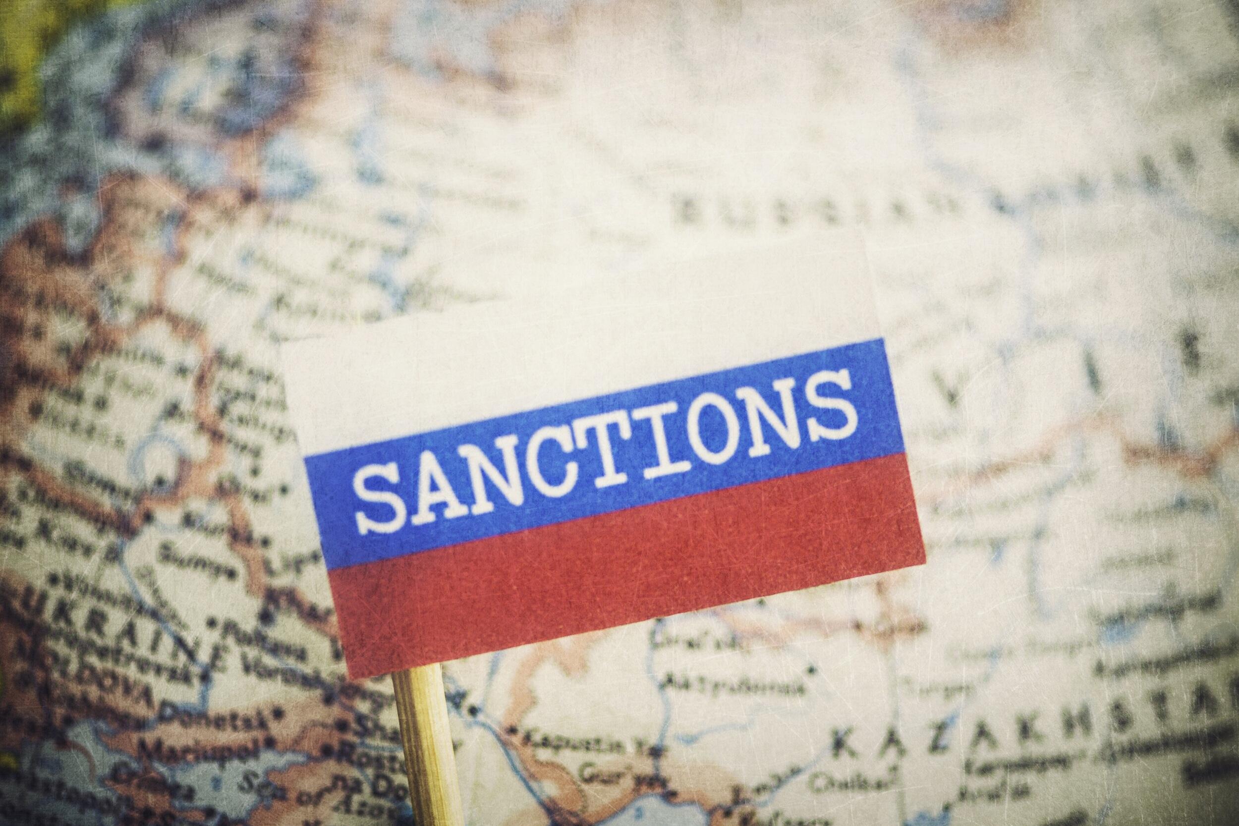 A Russian Flag that says \"Sanctions\" on it over a globe showing the country of Russia