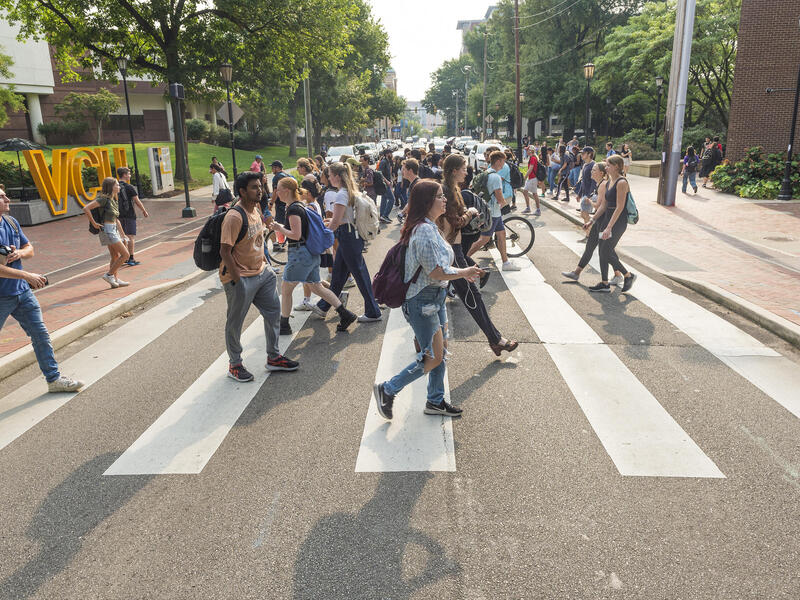 A photo of a crowd of people walking across a pedestrian corssing in the road. 