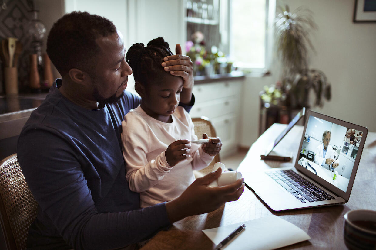 A father and daughter participate in a virtual telemedicine meeting.
