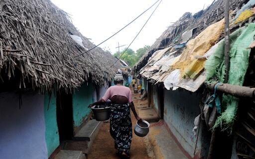 A woman walking between huts in a refugee camp