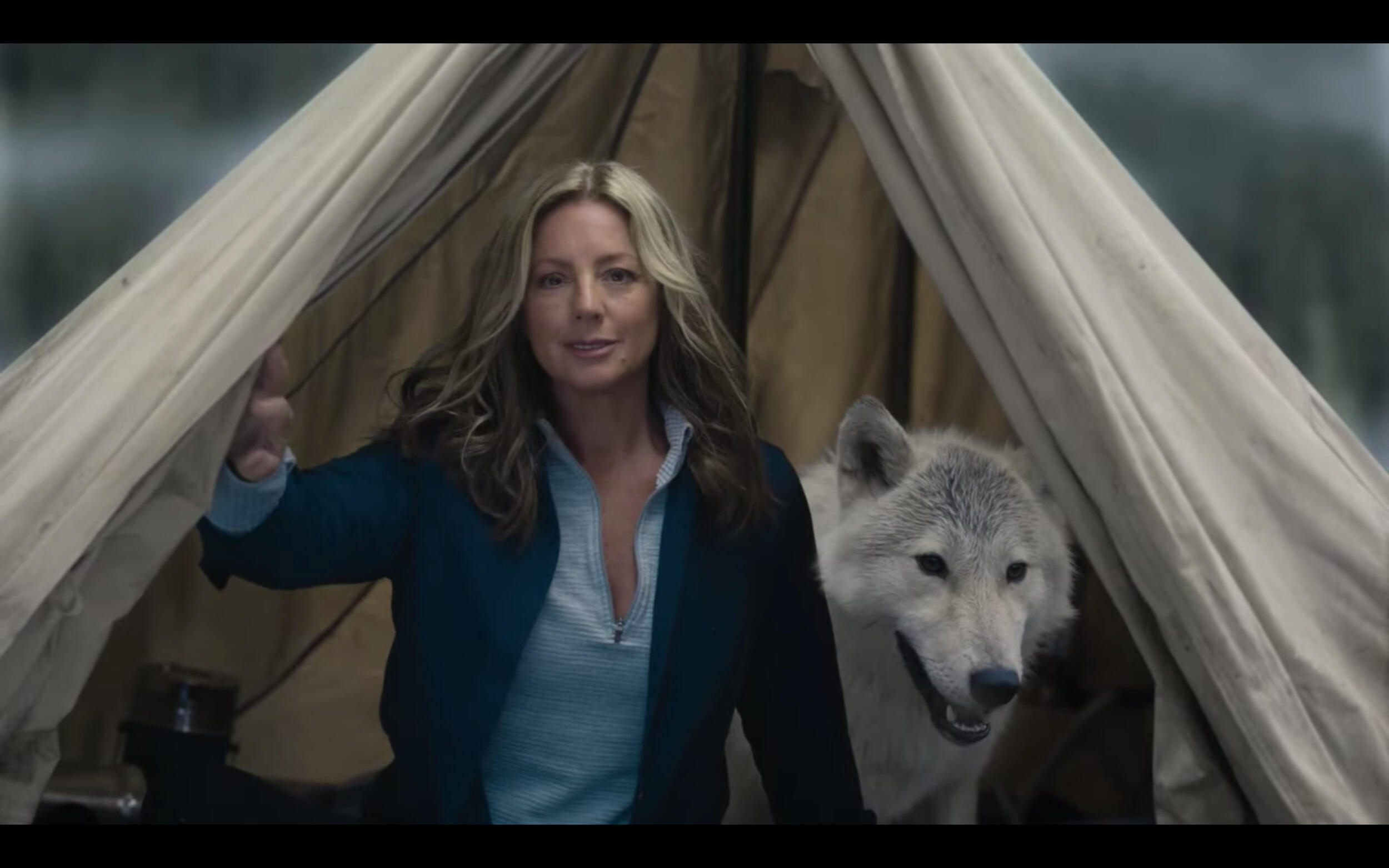 A woman standing in the middle of an open tent with a white and gray wolf standing behind her. 