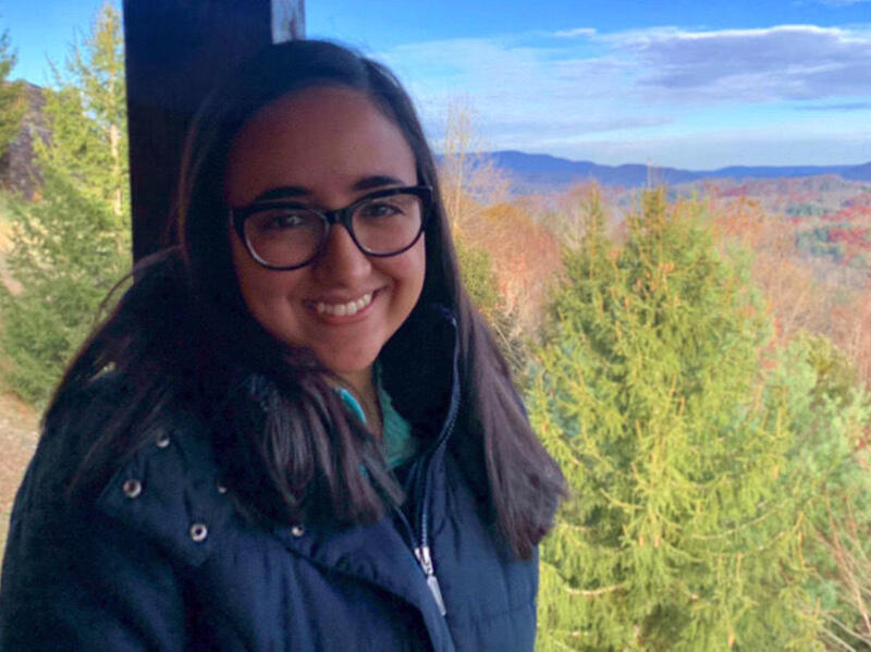 A person posing for a portrait with trees and hills in the background.
