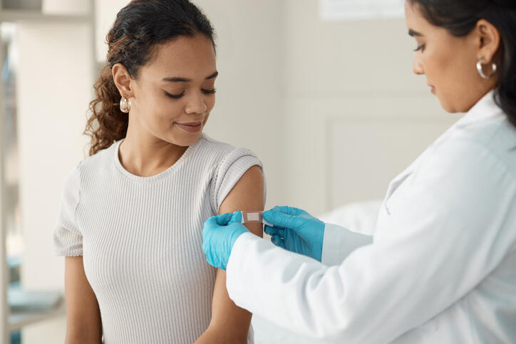 A photo of a doctor putting a bandaid on a woman's upper arm. 