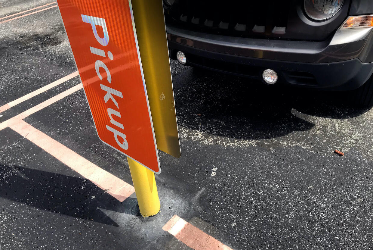 A car parked in front of a sign that says \"pickup.\"