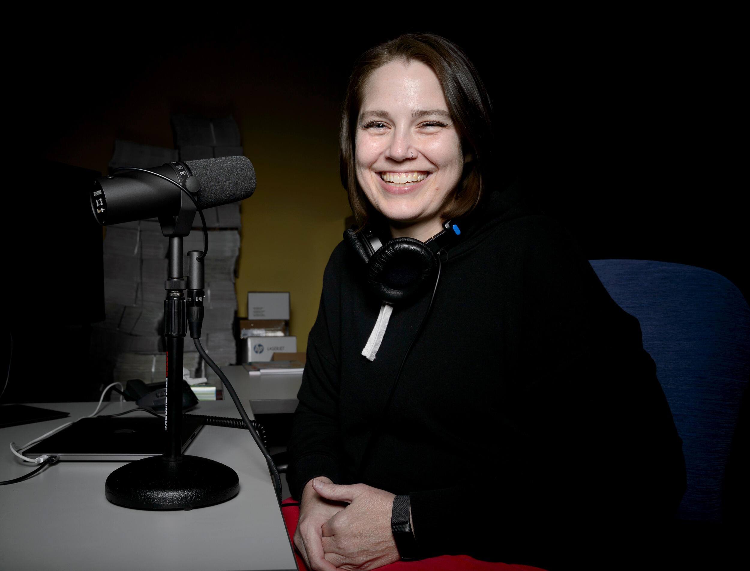 A woman sitting at a desk with a microphone on it and headphones around her neck. 