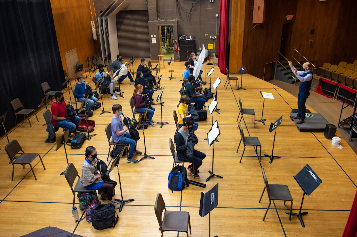 a wind ensemble rehearses during the COVID-19 pandemic, as musicians and the conductor wear masks