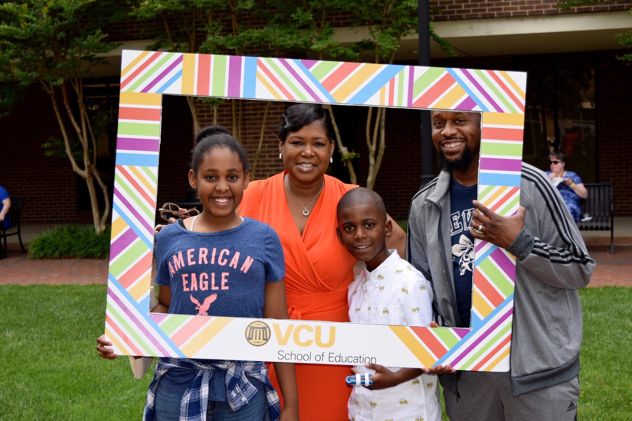 A family pose behind a picture frame with "V C U School of Education" printed on it.
