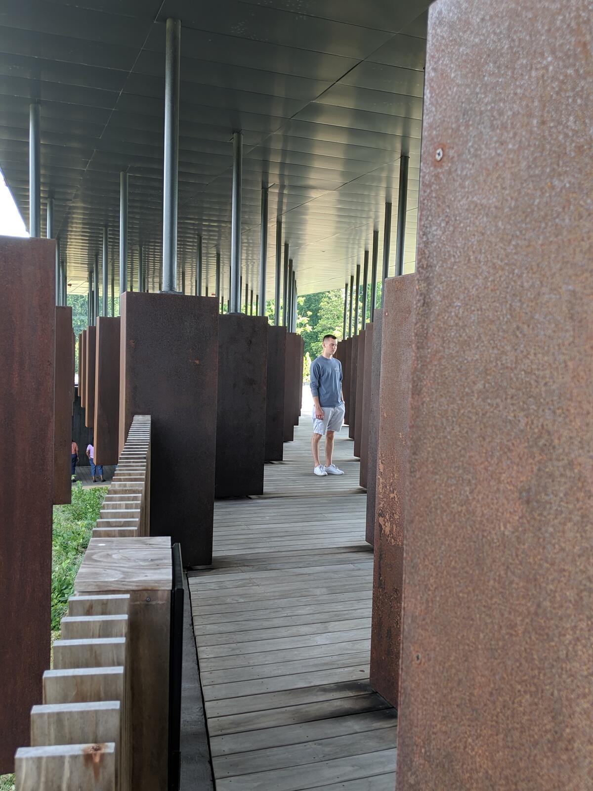 VCU student Alex Cornbrooks standing among the columns comprising the National Memorial for Peace and Justice.