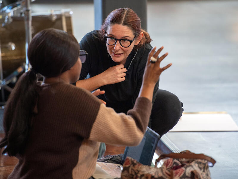 A photo of two women talking to each other while sitting and kneeling on the floor. 