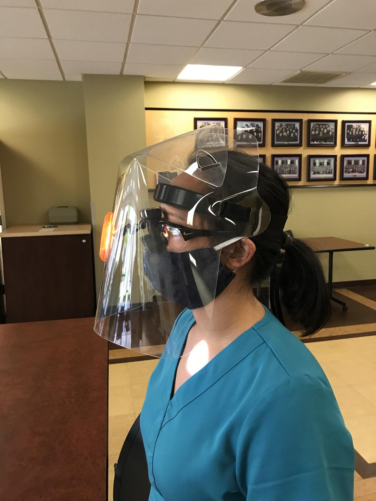 A person wearing a face shield, protective mask, and a pair of microscopic eyeglasses.