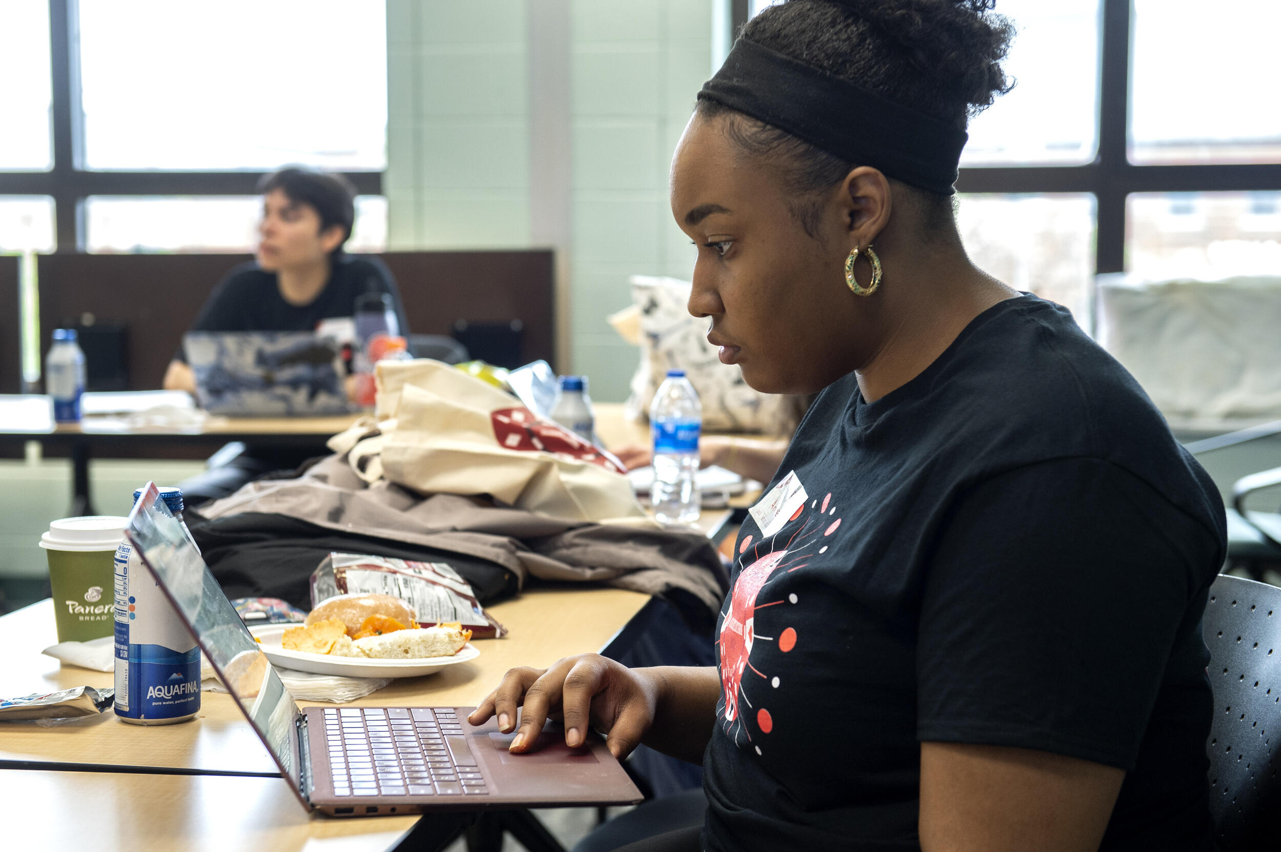 A student looking at a laptop with food next to her